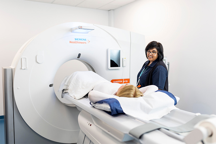Radiographer discussing CT scan with patient lying on bed of CT.