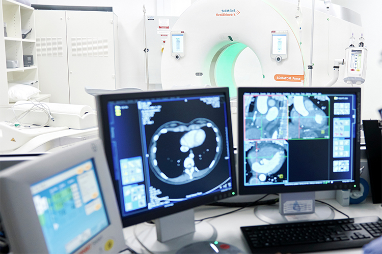 Patient CT images on computer screen with CT machine in background.